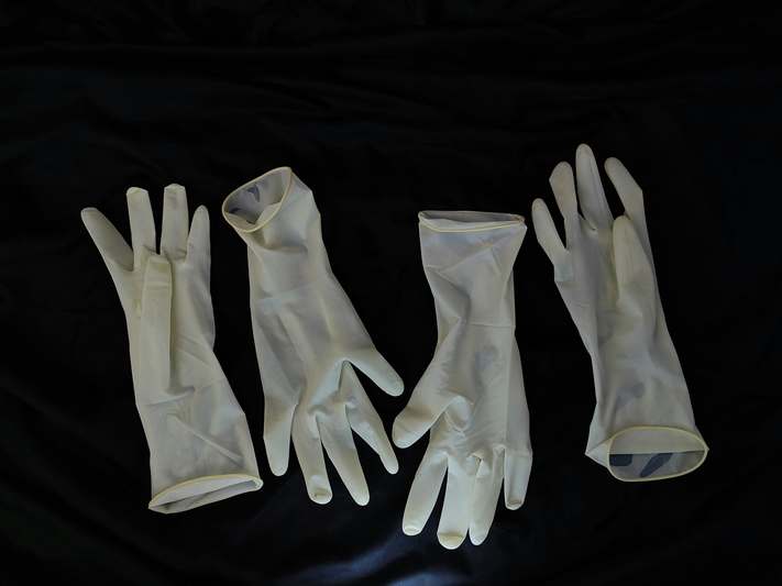 Hand holding a pair of textured, earth-toned reusable gloves next to a hanging wooden rack with labeled care instructions